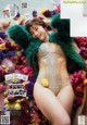 A woman laying on a bed of flowers wearing a green fur coat.