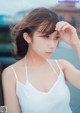 A woman in a white tank top leaning against a car.